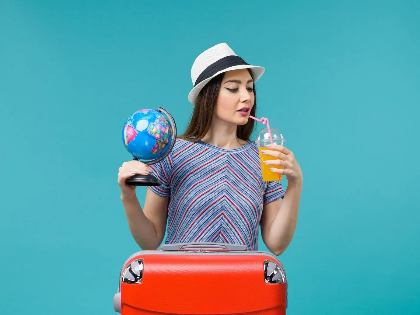 Vorderansicht einer Frau im Urlaub, die Saft und einen Globus vor blauem Hintergrund hält; Seereise, Urlaub, Sommertrip, Reise.